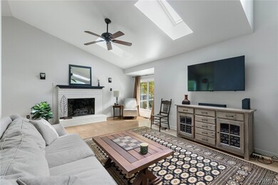 Living room with wood-type flooring, ceiling fan, lofted ceiling with skylight, and a brick fireplace
