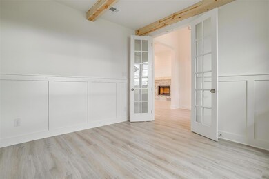 Empty room with beam ceiling, french doors, light wood-type flooring, and a fireplace