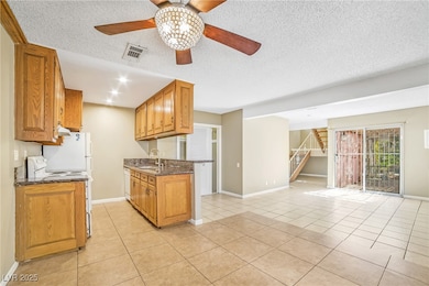 Kitchen with light tile patterned floors, white appliances, open floor plan, dark stone countertops, and brown cabinets