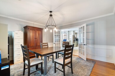 Dining space featuring ornamental molding, french doors, wainscoting, light wood-style floors, and a chandelier
