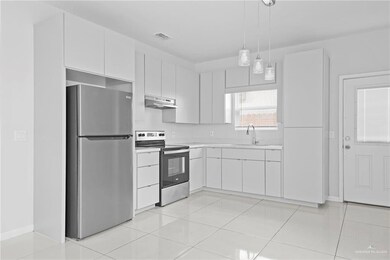 Kitchen featuring pendant lighting, light tile patterned flooring, sink, stainless steel appliances, and white cabinets