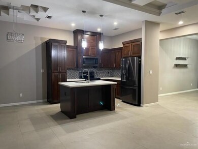 Kitchen featuring sink, decorative light fixtures, black refrigerator with ice dispenser, a center island with sink, and backsplash