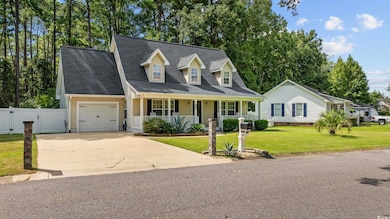 New england style home featuring a porch, a shingled roof, concrete driveway, a garage, and a gate