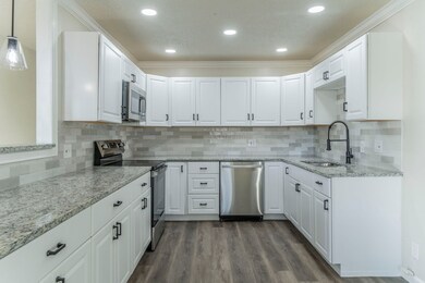 Kitchen with light stone countertops, appliances with stainless steel finishes, crown molding, white cabinetry, and tasteful backsplash
