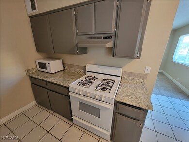 Kitchen featuring gray cabinetry, white appliances, under cabinet range hood, light tile patterned floors, and light stone countertops