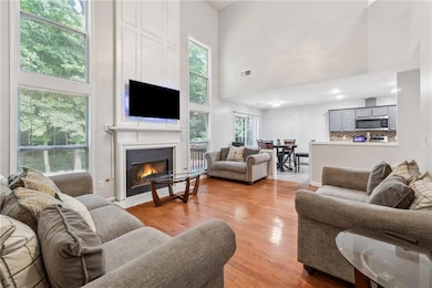 Living room with a towering ceiling, a warm lit fireplace, healthy amount of natural light, and light wood-type flooring