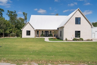 Modern farmhouse style home featuring brick siding, a porch, a front lawn, and a metal roof