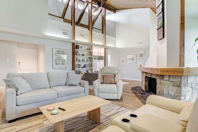 Living room featuring light wood-type flooring, high vaulted ceiling, ceiling fan, a fireplace with raised hearth, and beamed ceiling