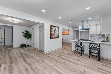 Kitchen featuring island exhaust hood, light countertops, light wood-style floors, white cabinets, and recessed lighting
