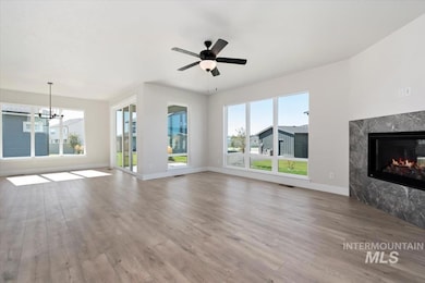 Unfurnished living room featuring light wood-style floors, a high end fireplace, ceiling fan, and a chandelier