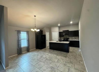 Kitchen with dark cabinetry, tasteful backsplash, black appliances, a center island with sink, and lofted ceiling