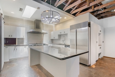 Kitchen featuring backsplash, stainless steel refrigerator, white cabinetry, concrete flooring, and recessed lighting