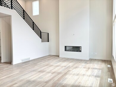 Unfurnished living room featuring a towering ceiling, light wood-style floors, a glass covered fireplace, and stairway