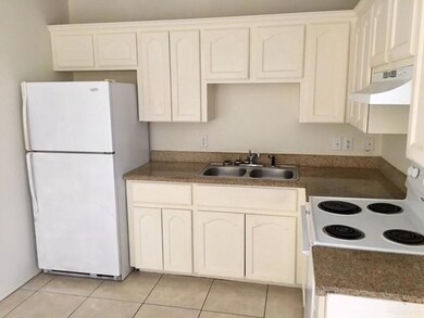 Kitchen featuring white appliances, under cabinet range hood, light tile patterned floors, and dark countertops