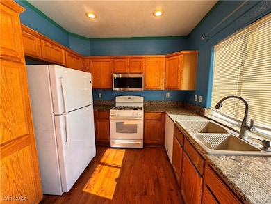 Kitchen featuring white appliances, dark wood finished floors, brown cabinetry, recessed lighting, and dark stone counters
