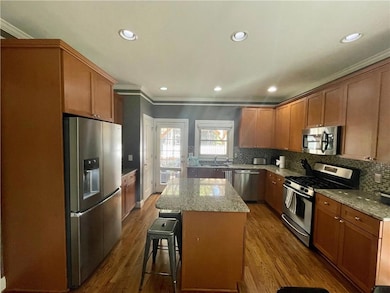 Kitchen with appliances with stainless steel finishes, crown molding, a kitchen island, backsplash, and dark wood-style floors