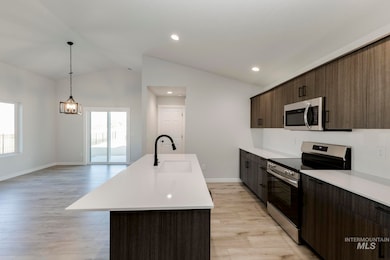 Kitchen with appliances with stainless steel finishes, vaulted ceiling, a center island with sink, dark brown cabinets, and light wood-style flooring