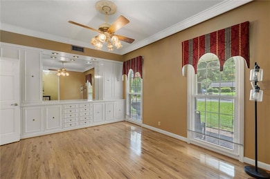 Empty room featuring ornamental molding, healthy amount of natural light, light wood finished floors, and ceiling fan