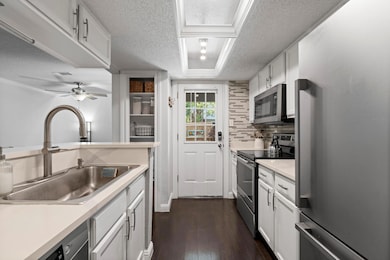 Kitchen with appliances with stainless steel finishes, light countertops, white cabinets, a textured ceiling, and dark wood-type flooring