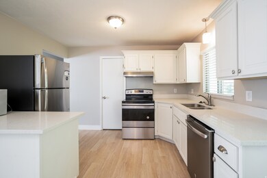 Kitchen with stainless steel appliances, light stone counters, hanging light fixtures, light wood-type flooring, and white cabinets