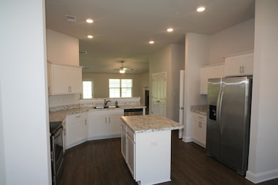 Kitchen with stainless steel appliances, dark wood-type flooring, a ceiling fan, a kitchen island, and white cabinetry