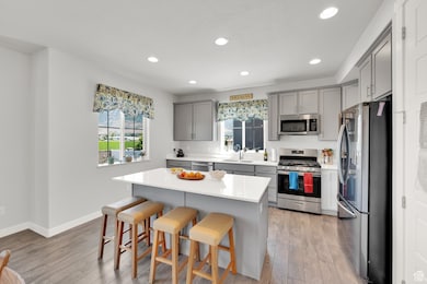 Kitchen with appliances with stainless steel finishes, gray cabinets, a kitchen bar, light wood-style flooring, and recessed lighting