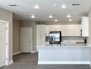 Kitchen with white cabinets, stainless steel appliances, dark wood-style floors, a peninsula, and light stone countertops