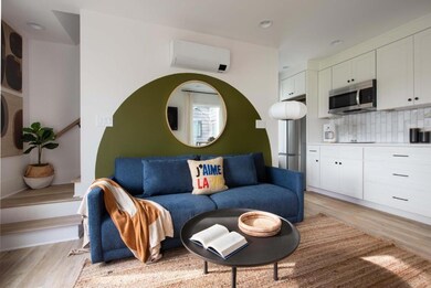 Living area with an AC wall unit, light wood-style floors, and recessed lighting