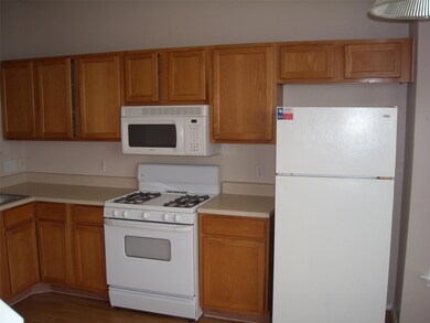 Kitchen with white appliances, light countertops, brown cabinetry, and dark wood-style flooring