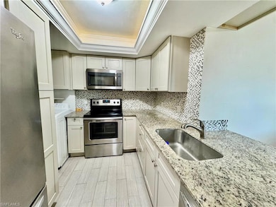 Kitchen with stainless steel appliances, a raised ceiling, a sink, washer / dryer, and ornamental molding