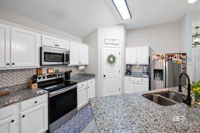 Kitchen with appliances with stainless steel finishes, white cabinetry, dark stone counters, backsplash, and pendant lighting