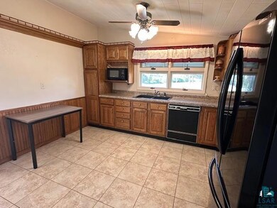 Kitchen with black appliances, a sink, brown cabinets, a ceiling fan, and a wainscoted wall