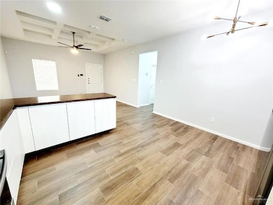 Unfurnished room featuring baseboards, light wood-style floors, visible vents, coffered ceiling, and ceiling fan with notable chandelier