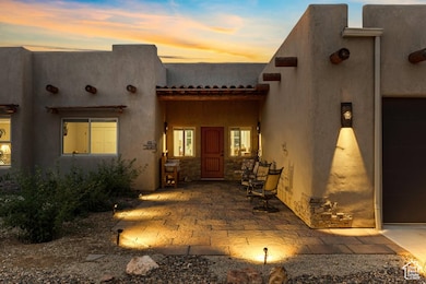 Exterior entry at dusk featuring stucco siding, stone siding, an attached garage, and a patio