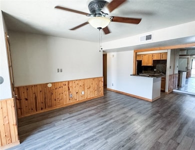 Unfurnished living room with wood walls, a ceiling fan, dark wood finished floors, and wainscoting