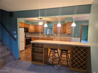 Kitchen with open shelves, a breakfast bar area, stainless steel range with electric cooktop, hanging light fixtures, and freestanding refrigerator