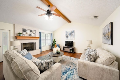 Living area featuring a textured ceiling, wood finished floors, a brick fireplace, and a ceiling fan