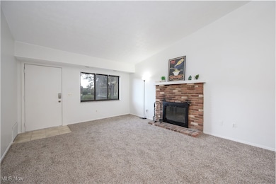 Unfurnished living room with a brick fireplace, light carpet, and vaulted ceiling