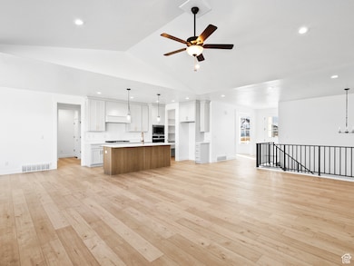 Kitchen with open floor plan, white cabinets, light countertops, a center island with sink, and decorative light fixtures