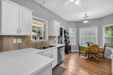 Kitchen with a sink, stainless steel dishwasher, light countertops, white cabinetry, and decorative backsplash
