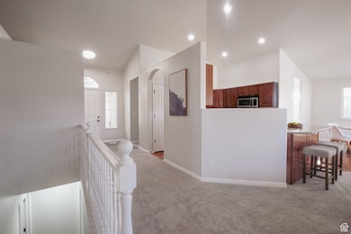 Hall featuring vaulted ceiling, light carpet, arched walkways, an upstairs landing, and healthy amount of natural light