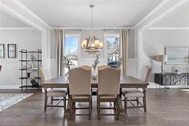 Dining space featuring dark wood-style floors, a notable chandelier, ornamental molding, and wainscoting