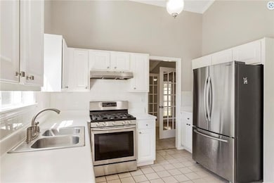 Kitchen with appliances with stainless steel finishes, under cabinet range hood, a sink, light countertops, and decorative backsplash