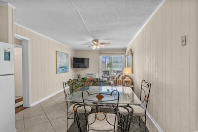 Dining space with ceiling fan, light tile patterned floors, ornamental molding, a textured ceiling, and wood walls