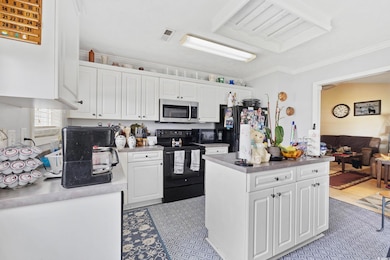 Kitchen featuring electric range, stainless steel microwave, freestanding refrigerator, white cabinets, and crown molding