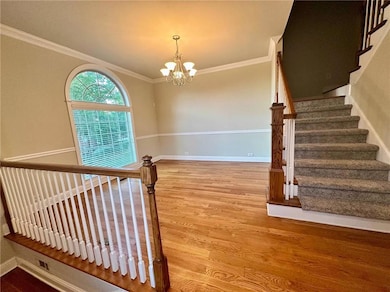 Stairway with wood finished floors, a chandelier, baseboards, and ornamental molding