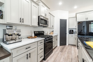 Kitchen featuring black gas range, stainless steel microwave, light wood-style floors, recessed lighting, and white cabinets