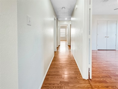 Hallway featuring light wood finished floors, a textured ceiling, and a textured wall