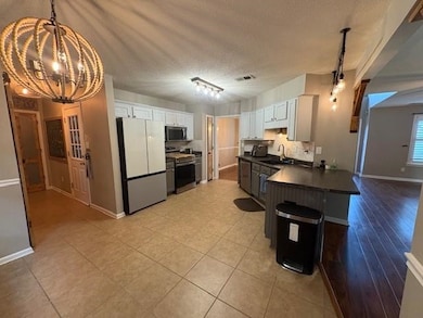 Kitchen with stainless steel appliances, a chandelier, dark countertops, white cabinetry, and hanging light fixtures