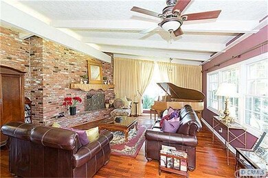Formal living room with brick fireplace, beamed ceiling and windows that allow natural light into the room.